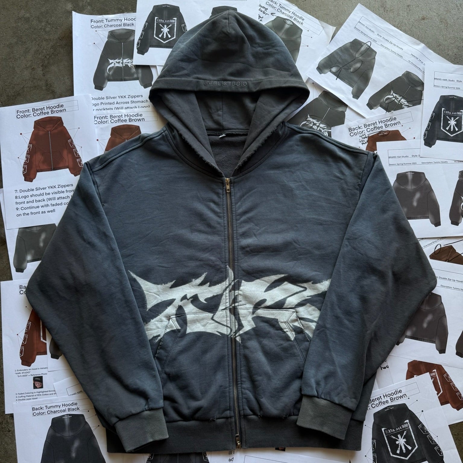 Gray hoodie with a graphic design on a surface with printed materials.